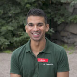 Porträtt av Filip Saxena som sitter ner i läkarkläder och ler mot kameran