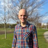 Porträttbild av Johan Theander som står vid en grön gräsmatta framför ett träd